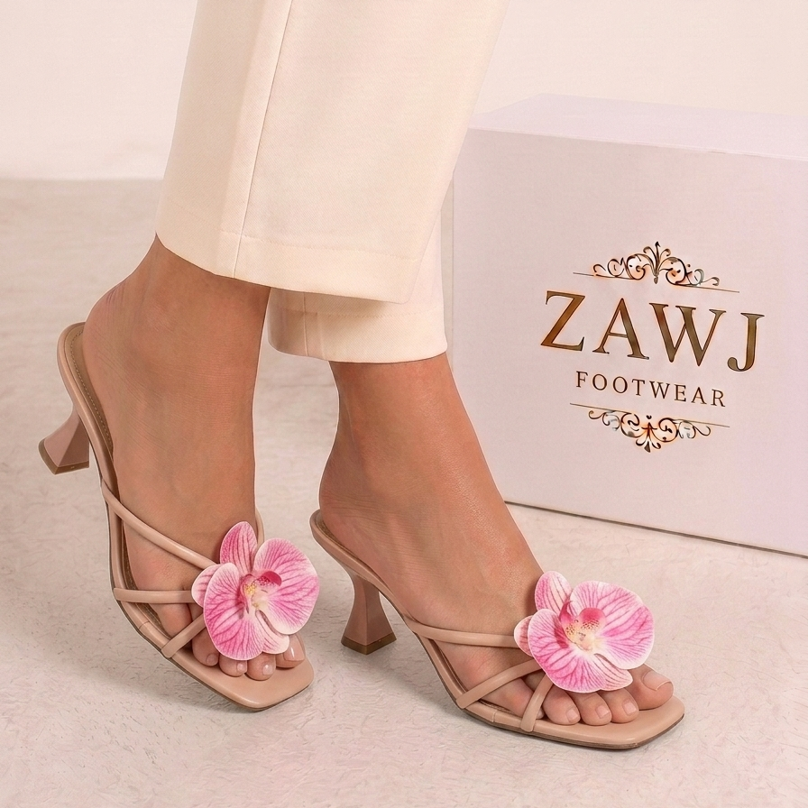 Beige high-heeled sandals with pink floral decorations worn by a person, with ZAWJ Footwear box in the background.